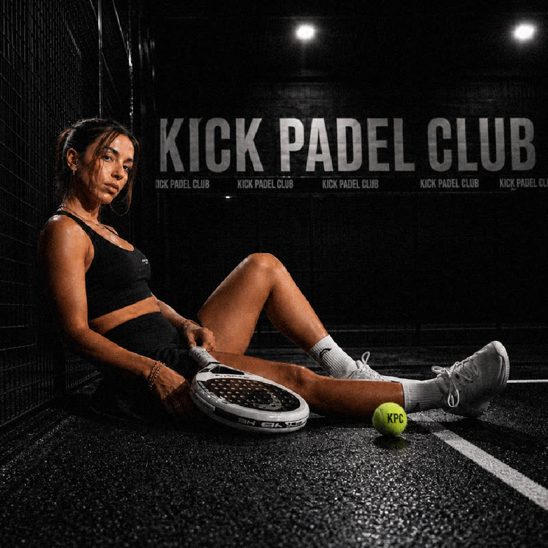 Woman sitting courtside with her padel racket and a Kick Padel Club branded ball, in front of a Kick Padel Club wall graphic